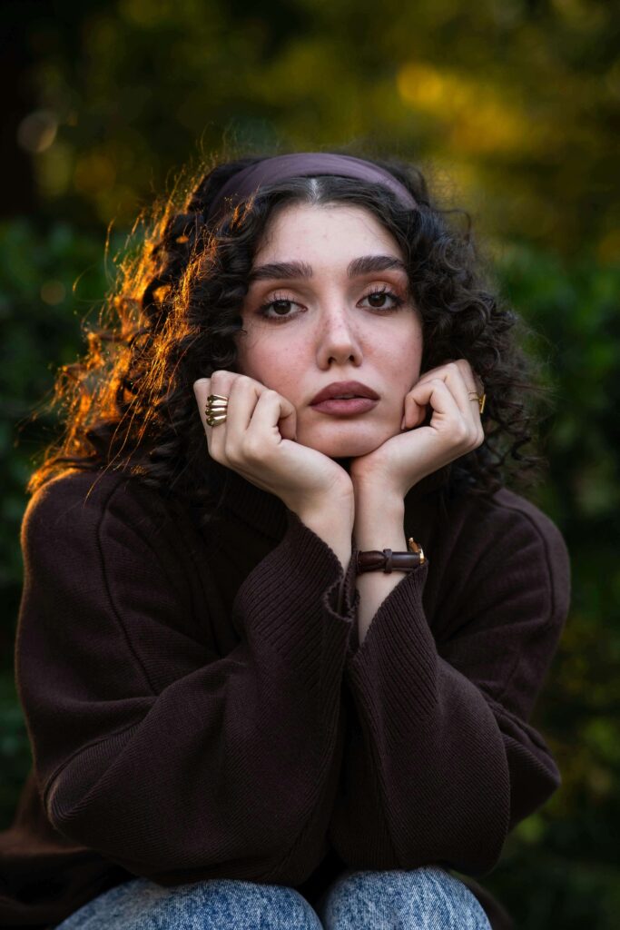 A young woman resting her face on her hands while looking thoughtful, illustrating self-reflection and emotional awareness. Improve the quality of your relationships and heal your relationship with yourself with the support of a relationship therapist in Los Angeles, CA.