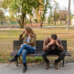 A couple sits on opposite ends of a park bench, both looking frustrated and distant, suggesting tension or conflict in their relationship. With relationship therapy in Los Angeles, CA you can begin to heal and cope with the anger affecting your relationship.