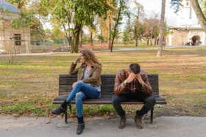 A couple sits on opposite ends of a park bench, both looking frustrated and distant, suggesting tension or conflict in their relationship. With relationship therapy in Los Angeles, CA you can begin to heal and cope with the anger affecting your relationship.