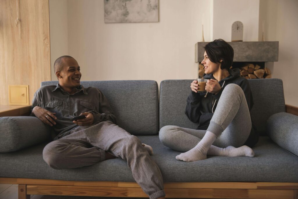 coffee | relationship therapist in los anegels, ca | relationship therapy | relationship communication skills | Encino | Tarzana | Sherman Oaks A couple sits on a couch at home, smiling and talking comfortably while sharing a warm moment together. Reconnect with ease and build healthier patterns of communication through relationship therapy in Los Angeles, CA.