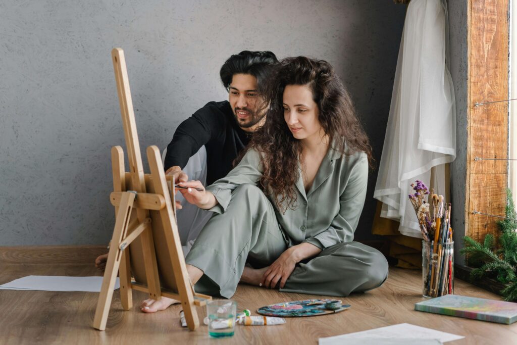 painting | relationship therapy in los angeles, ca | relationship therapist | relationship with self | Encino | Tarzana | Sherman Oaks A couple sitting on the floor painting together, collaborating closely while creating art. See how relationship therapy in Los Angeles, CA helps you rebuild trust and practice vulnerability so connection feels easier and more natural.