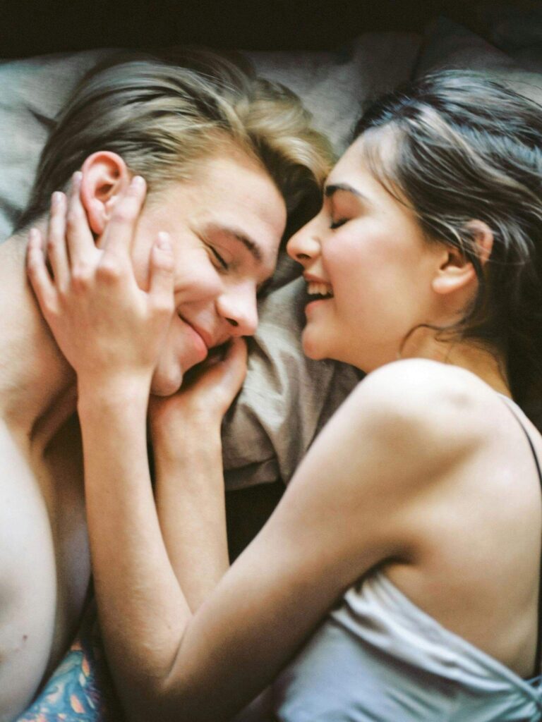 A couple lying close together, smiling and touching each other’s faces while sharing an intimate, tender moment. Learn how relationship therapy in Los Angeles, CA helps you open up emotionally and build deeper connection with the guidance of a skilled relationship therapist.