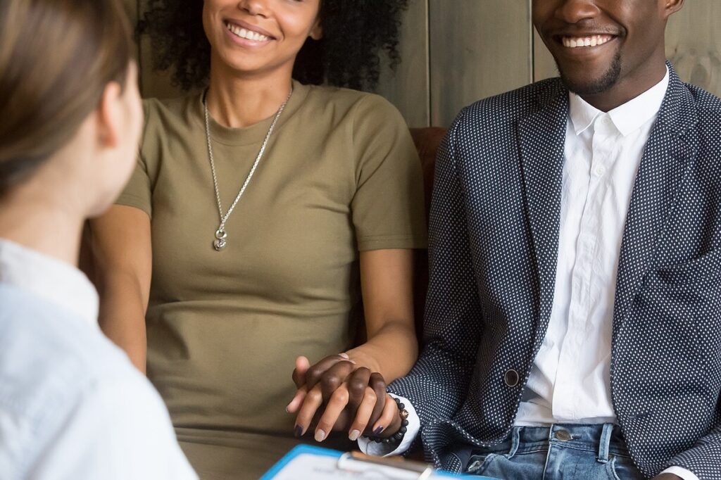Couple sitting side by side holding hands while speaking with a therapist in an office setting. Through guided support, relationship therapy in Los Angeles, CA helps partners feel heard, supported, and more connected.