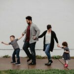 Balancing Parenthood and Partnership Without Losing Yourself Family of four holding hands while walking together along a sidewalk outdoors. Navigate parenting challenges and stay connected as partners with relationship therapy in Los Angeles, CA.