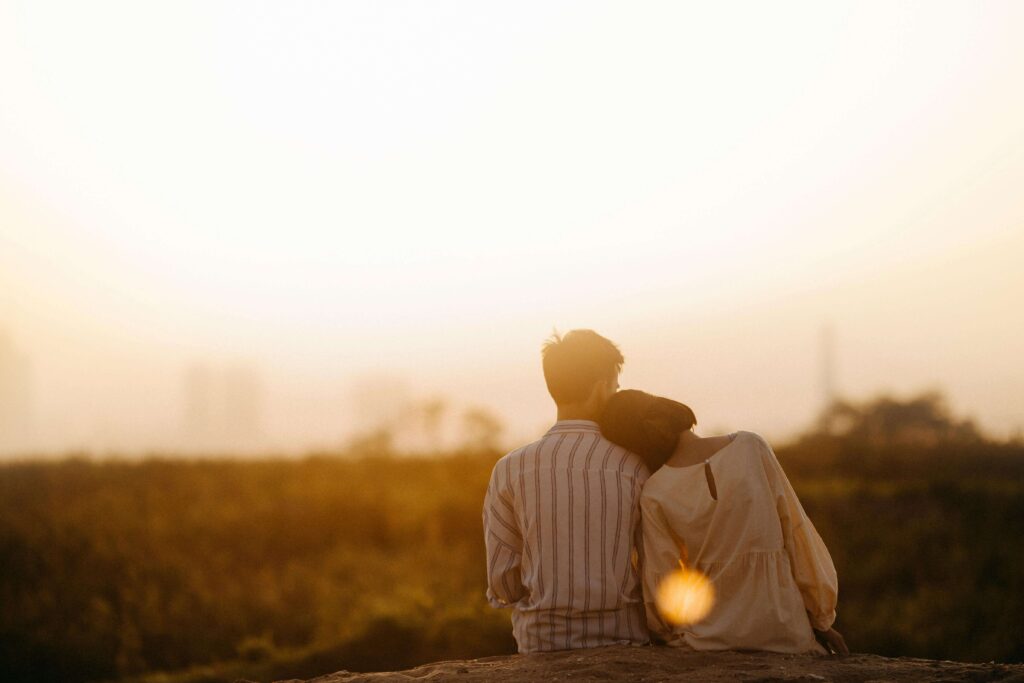 Couple sitting close together outdoors at sunset, leaning into each other while looking at the horizon. Reconnect emotionally and strengthen your partnership through relationship therapy in Los Angeles, CA during the transition into parenthood.