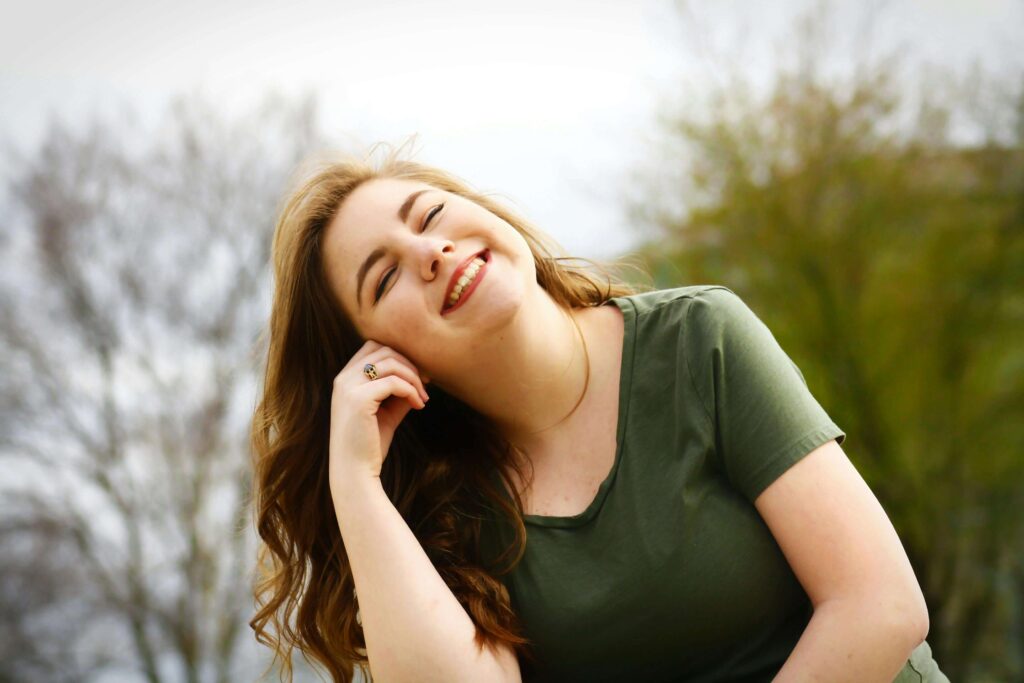 Joyful woman with long hair laughing outdoors in natural setting wearing green shirt. Stop abandoning yourself in relationships and reconnect with who you truly are through relationship therapy in Los Angeles, CA.