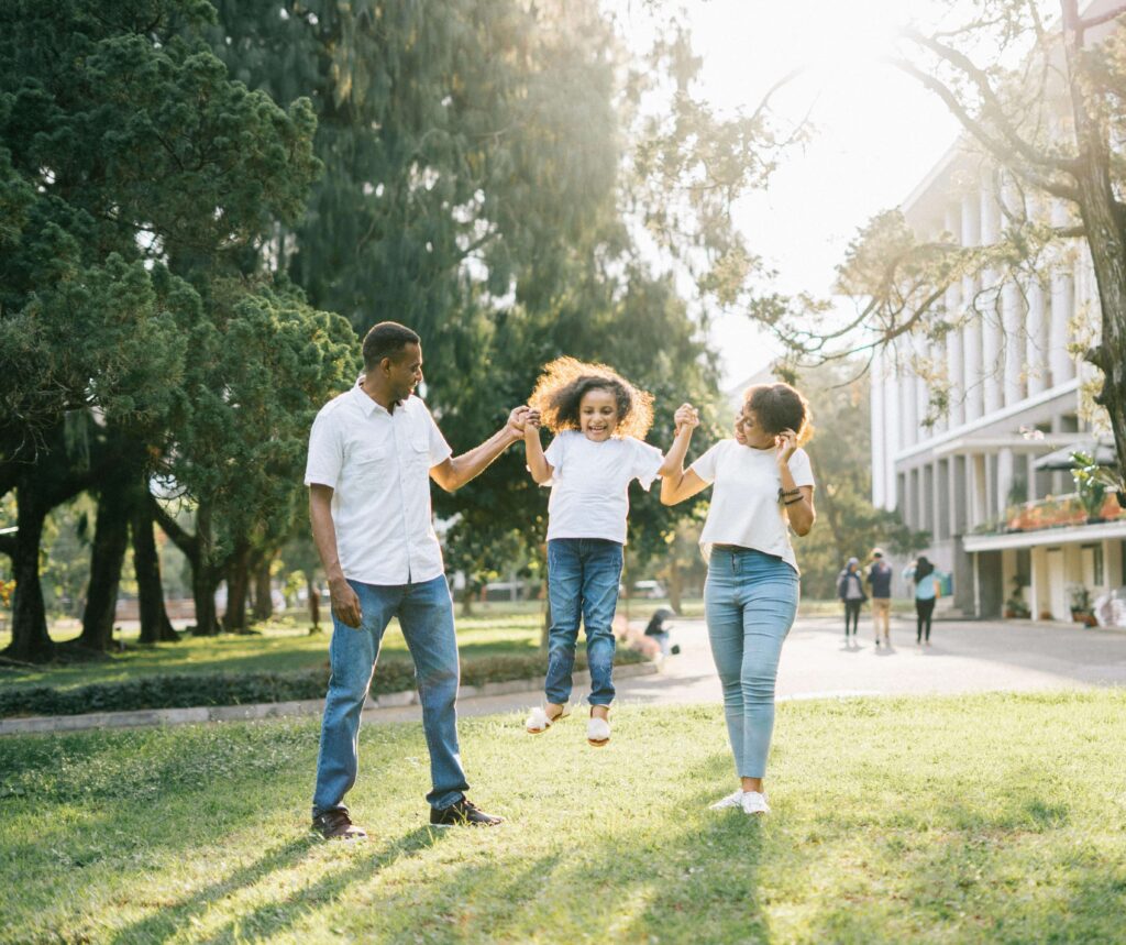 Parents holding hands with their child while walking together on a grassy campus pathway. Support your relationship as it evolves with the demands of family life through relationship therapy in Los Angeles, CA.