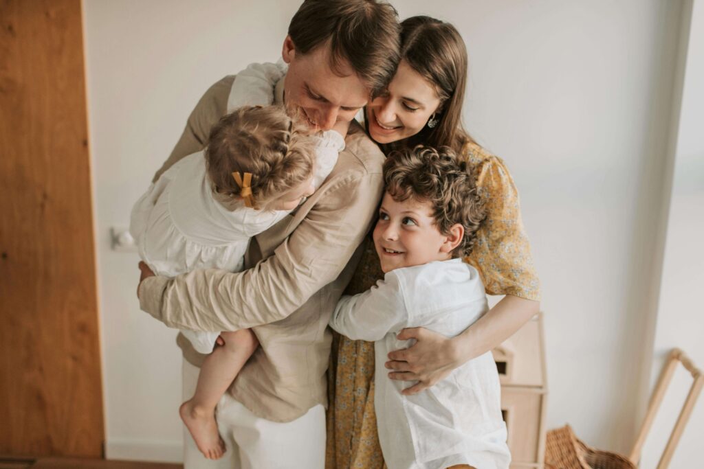 Parents embracing their two young children inside a softly lit home environment. Build emotional safety and connection as parents with the support of relationship therapy in Los Angeles, CA.