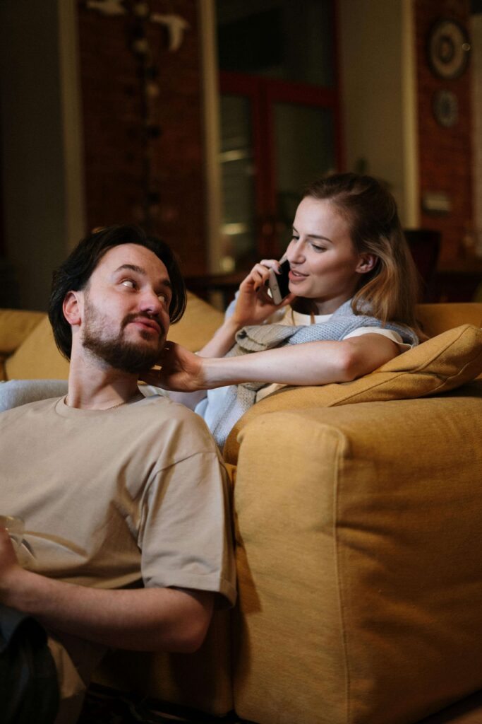 A woman on the phone while sitting on a couch with a man looking up at her. Discover how to honor your needs without guilt through relationship therapy in Los Angeles, CA.