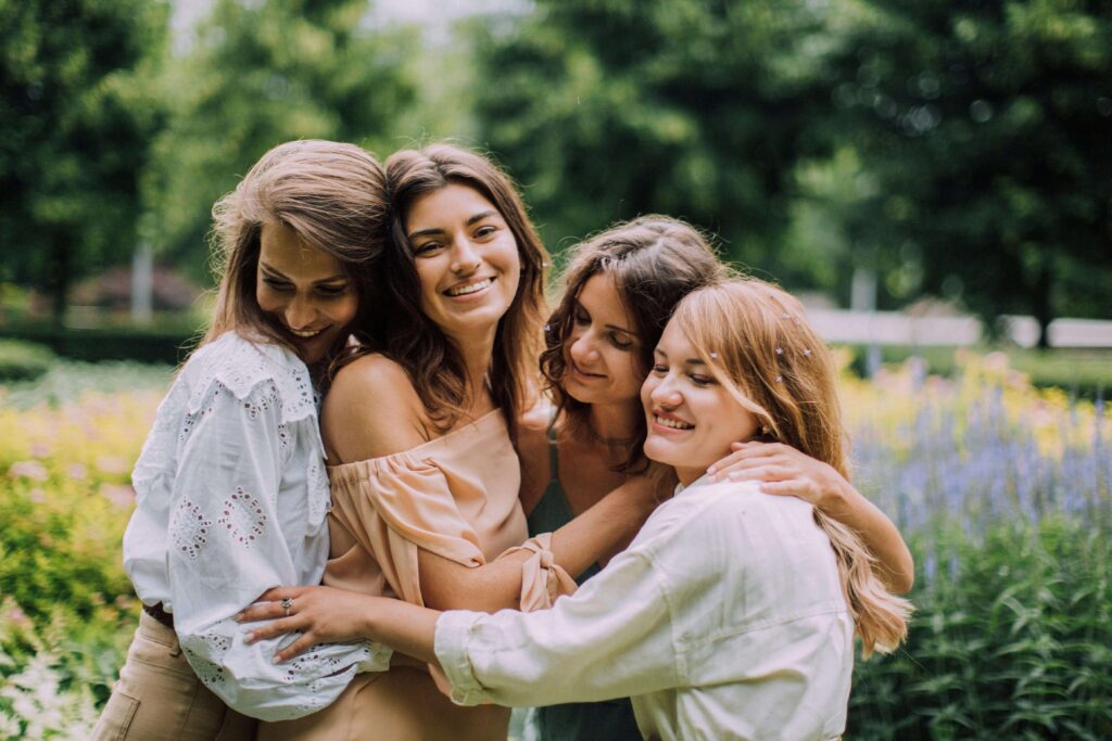 Four women embracing in a group hug outdoors in a sunny garden. Break free from repeating relationship patterns with relationship therapy in Los Angeles, CA.