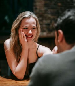 Woman laughing joyfully during conversation with person across from her at wooden table. Create healthier connections and genuine intimacy with relationship therapy in Los Angeles, CA.