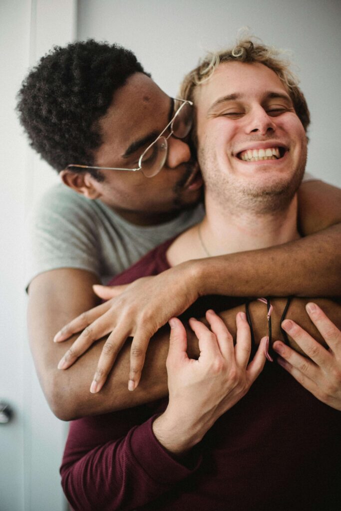 glasses | relationship therapy in Los Angeles, CA | relationship with self | relationship therapist | Encino | Tarzana | Sherman Oaks Two men embracing affectionately with one kissing the other's cheek. Rediscover vulnerability and closeness with support from relationship therapy in Los Angeles, CA.