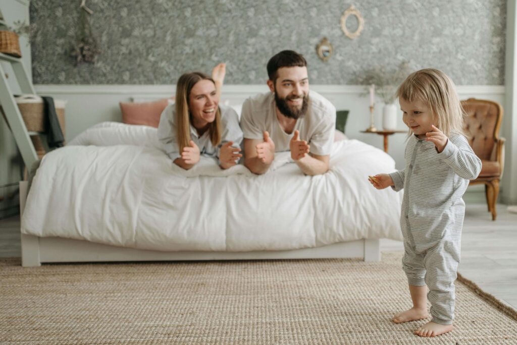 Parents lying on bed giving thumbs up to young child standing nearby in pajamas. Break old cycles and parent with clarity through relationship therapy in Los Angeles, CA.