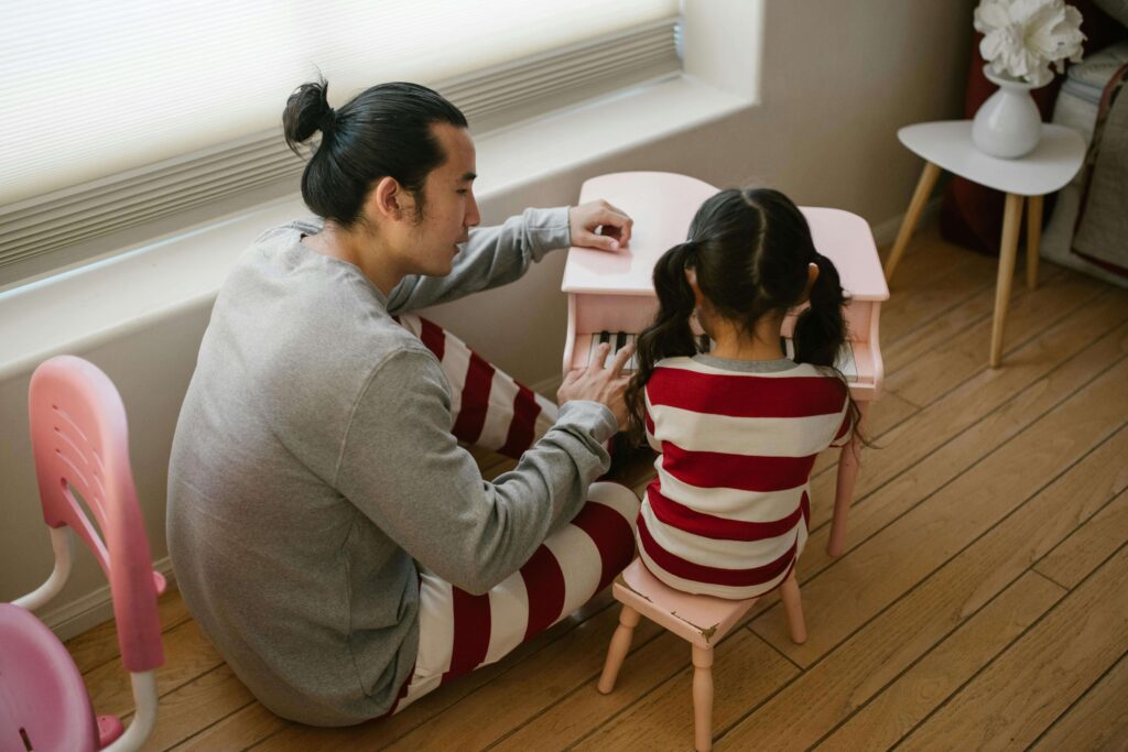 Father and daughter in matching striped shirts playing at pink piano together. Understand your triggers and build healthier relationships through relationship therapy in Los Angeles, CA.