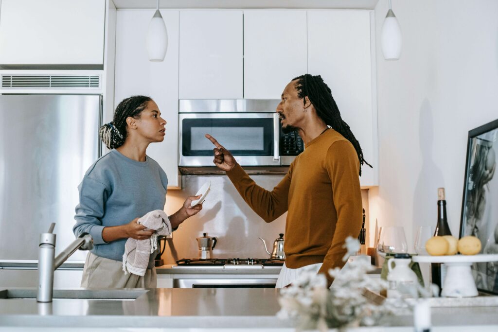 Couple arguing in kitchen with man gesturing while woman holds dish towel. Break the cycle of anger and uncover the hurt beneath conflict through relationship therapy in Los Angeles, CA.