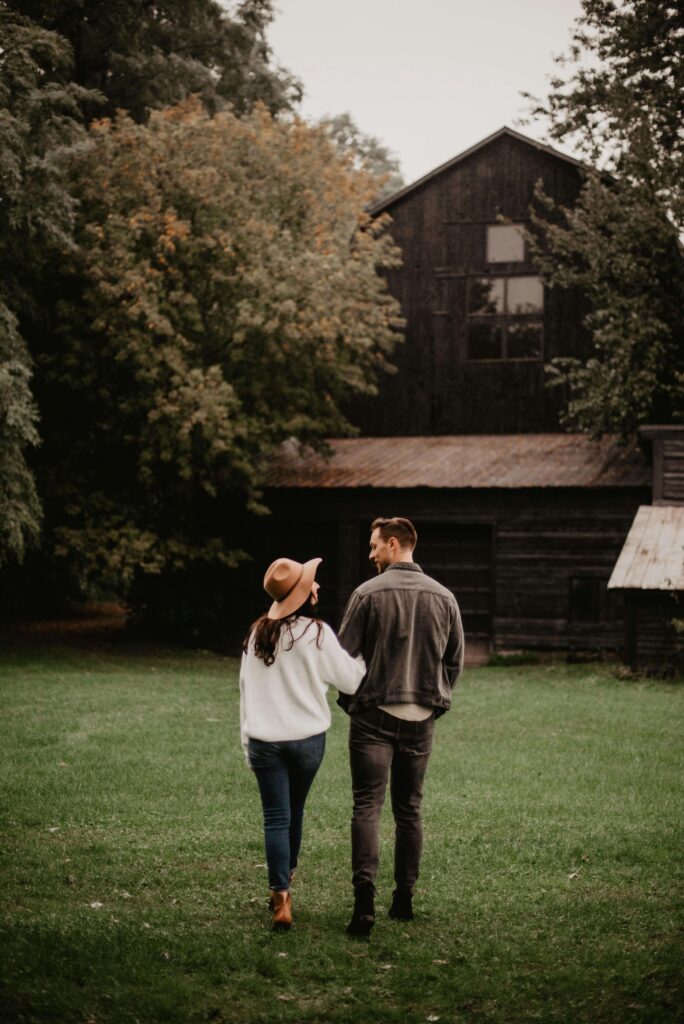 Couple walking away from camera across grass toward barn with trees. Transform reactive patterns into genuine understanding through relationship therapy in Los Angeles, CA.