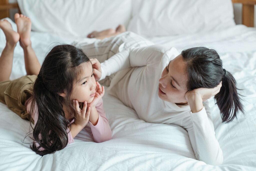 Mother and daughter lying on bed facing each other in conversation. Model emotional safety and repair for your children with support from relationship therapy in Los Angeles, CA.