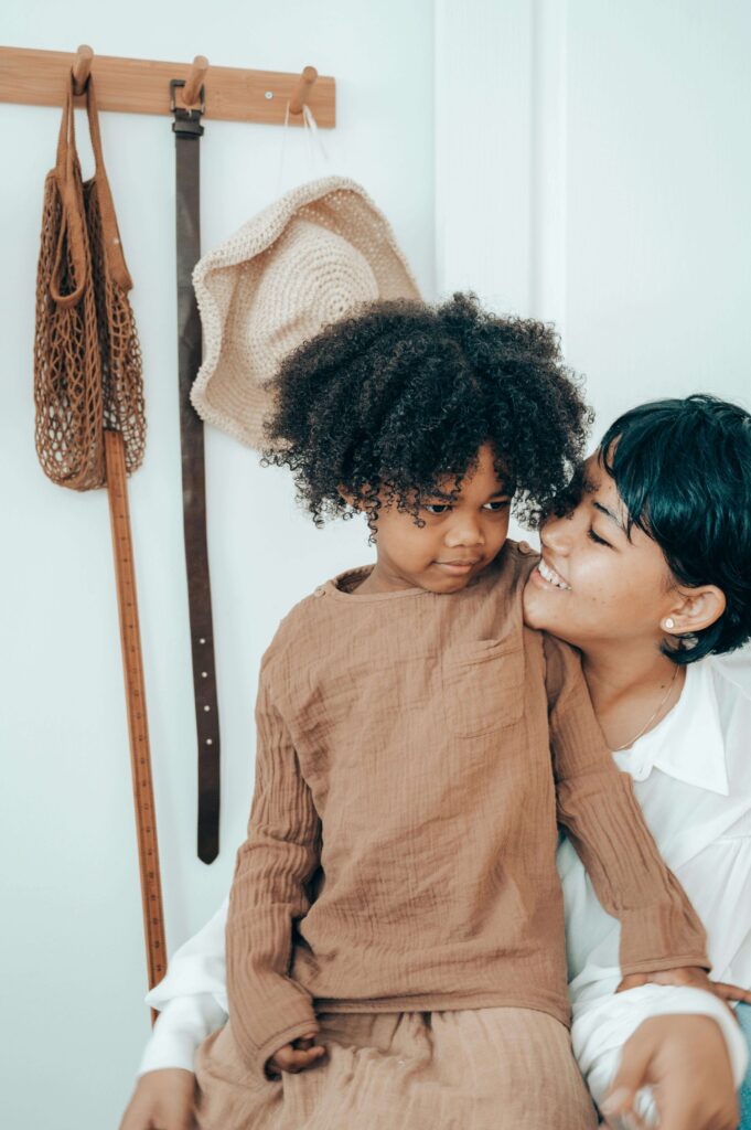 Mother kissing child on cheek while child looks away with neutral expression. Understanding your triggers helps you respond with intention through relationship therapy in Los Angeles, CA.
