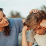 Teaching Kids About Emotions Starts With How We Handle Our Own Through Relationship Therapy Mother gently stroking son's hair while sitting together outdoors. Learn to regulate your emotions so your children can learn from you through relationship therapy in Los Angeles, CA.