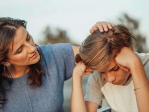 Mother gently stroking son's hair while sitting together outdoors. Learn to regulate your emotions so your children can learn from you through relationship therapy in Los Angeles, CA.