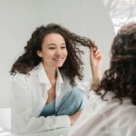 Woman smiling at herself in round mirror while touching her hair. Develop the self-awareness that transforms all your relationships through relationship therapy in Los Angeles, CA.