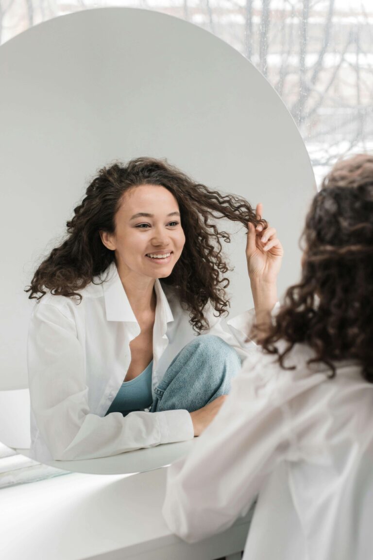 Woman smiling at herself in round mirror while touching her hair. Develop the self-awareness that transforms all your relationships through relationship therapy in Los Angeles, CA.