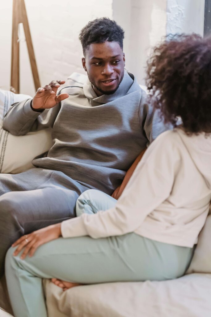 Man gesturing while speaking to his partner while sitting on a couch. Practice staying connected to yourself while staying in relationship through relationship therapy in Los Angeles, CA.