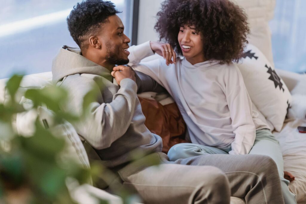 Couple smiling and talking closely on couch in casual clothing. Build intimacy based on who you actually are through relationship therapy in Los Angeles, CA.