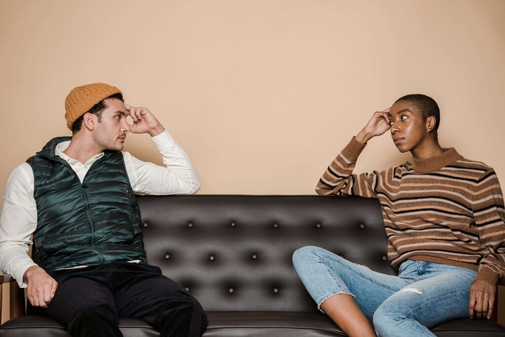 Couple sitting apart on black couch looking at each other thoughtfully. Explore vulnerability safely and express yourself without fear through relationship therapy in Los Angeles, CA.