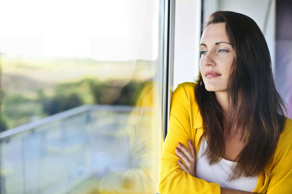 Woman in yellow cardigan looking thoughtfully out window. Learn to honor your needs without guilt through relationship therapy in Los Angeles, CA.